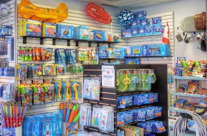 A store interior featuring colorful pool supplies, toys, and inflatables on display. Shelves are neatly arranged with various swimming and diving accessories.
