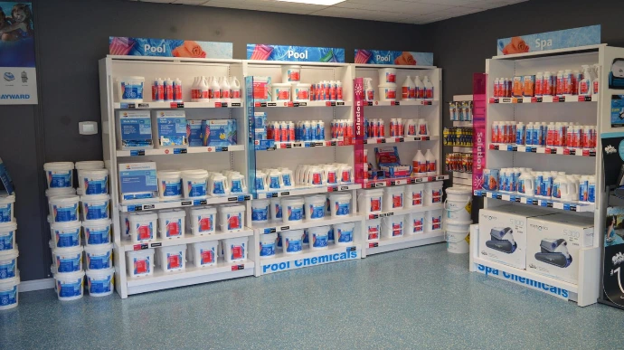 A store interior with shelves displaying pool and spa chemicals, cleaning supplies, and associated equipment in a brightly lit space.
